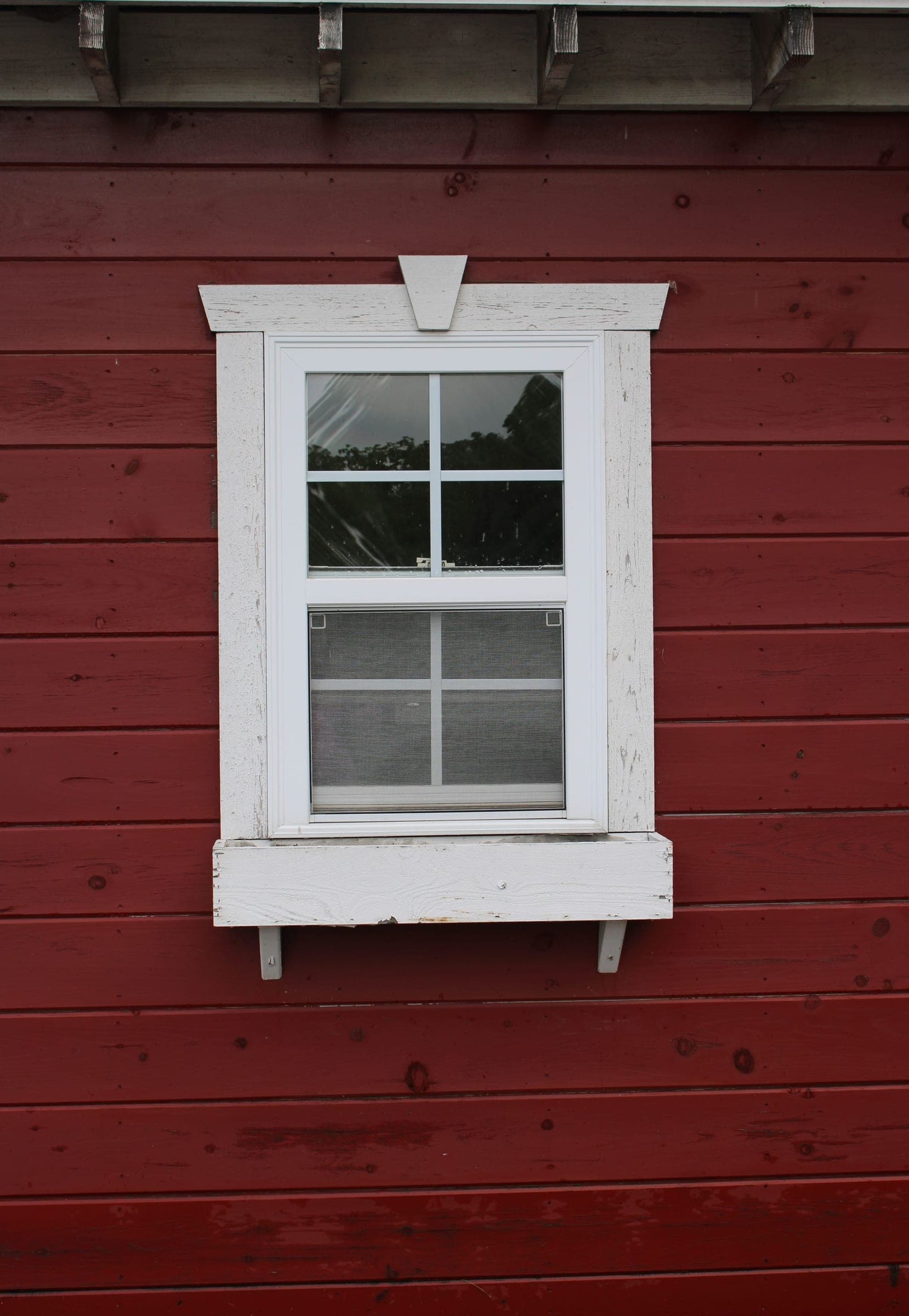 White hung window with trim on red wood siding