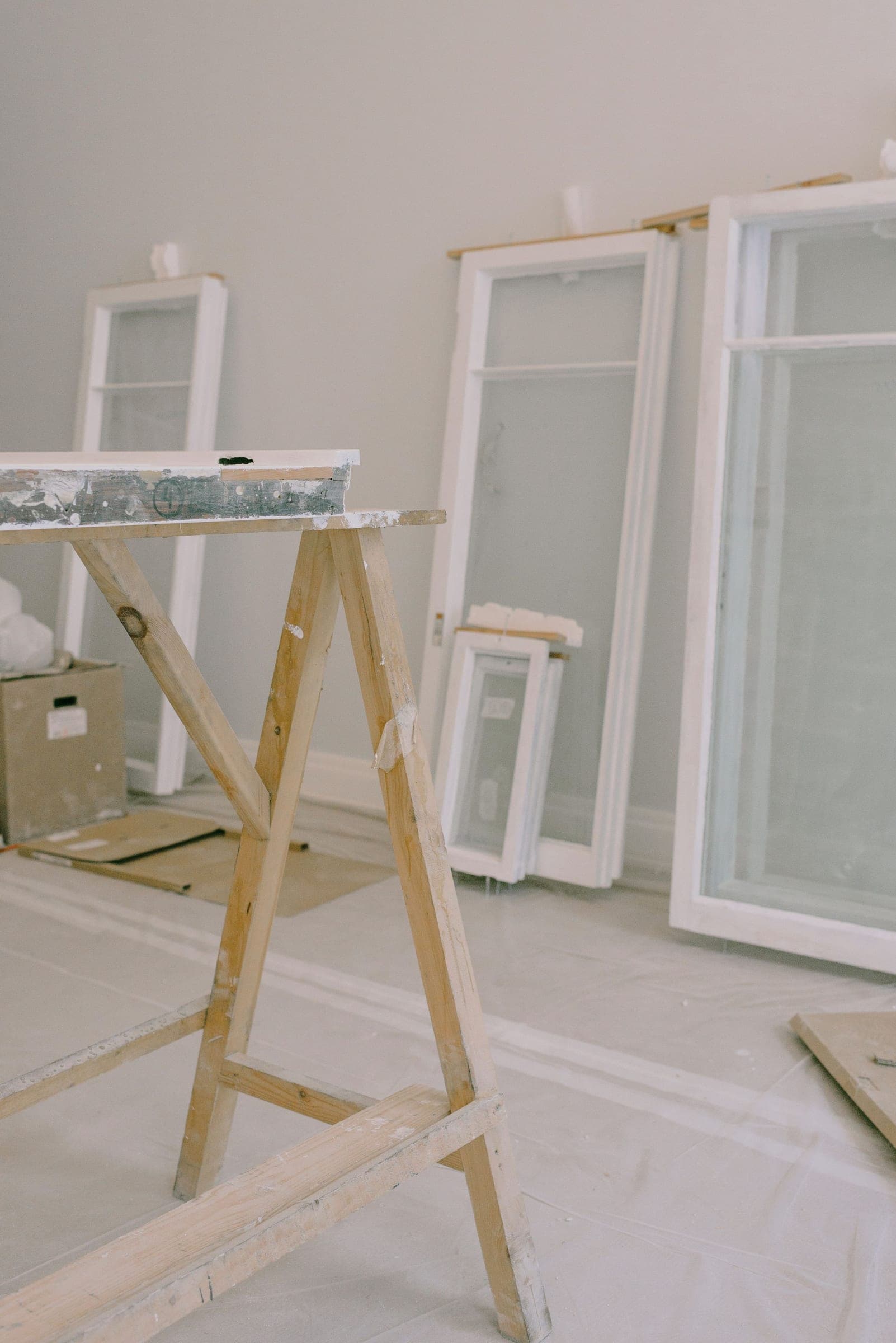 New white window units leaning against the wall beside a sawhorse, ready to install