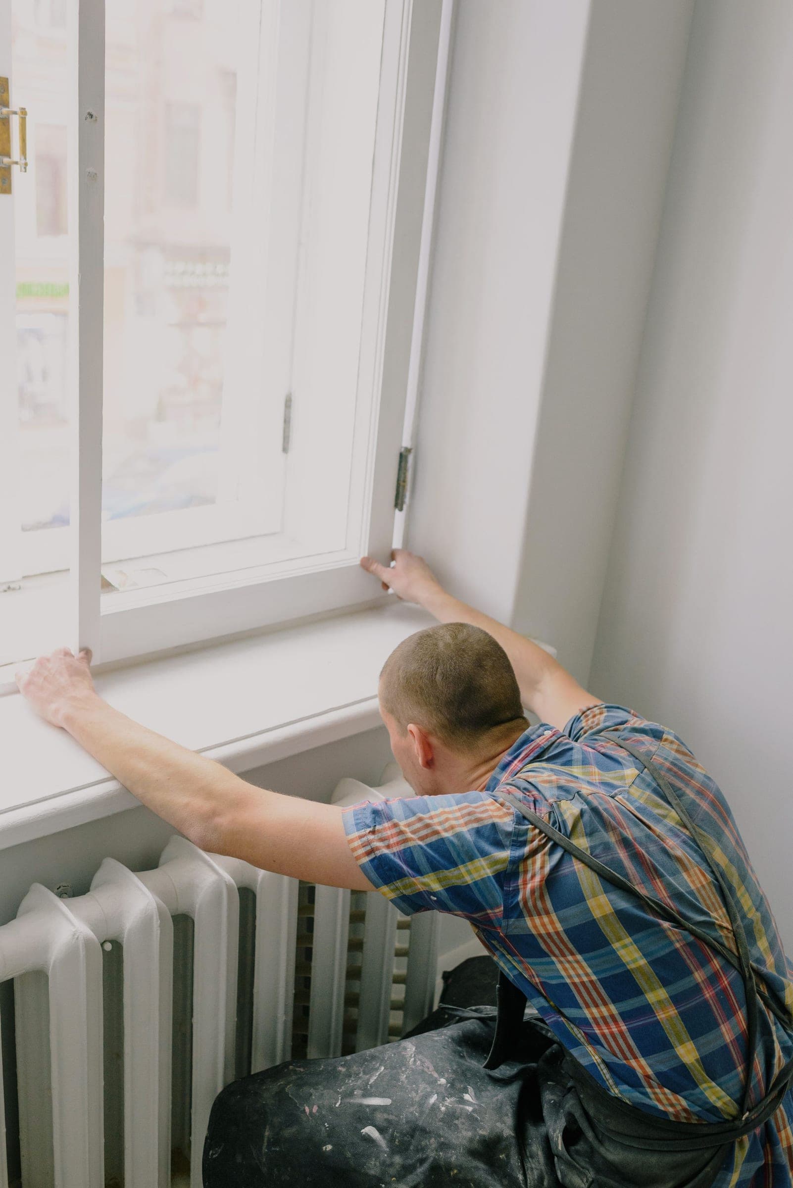 Installer fitting a new white window frame against the sill inside a bright room